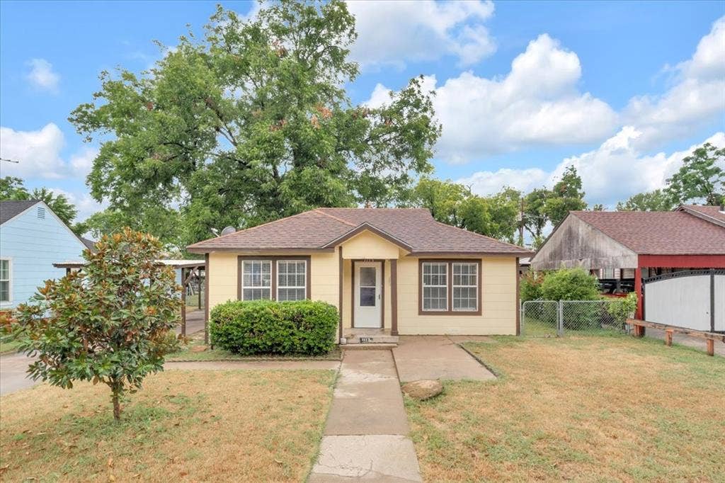 1113 Hudgins Avenue, Fort Worth, TX 76111 Single-story residence featuring light yellow siding, brown trim, and a brown shingle roof