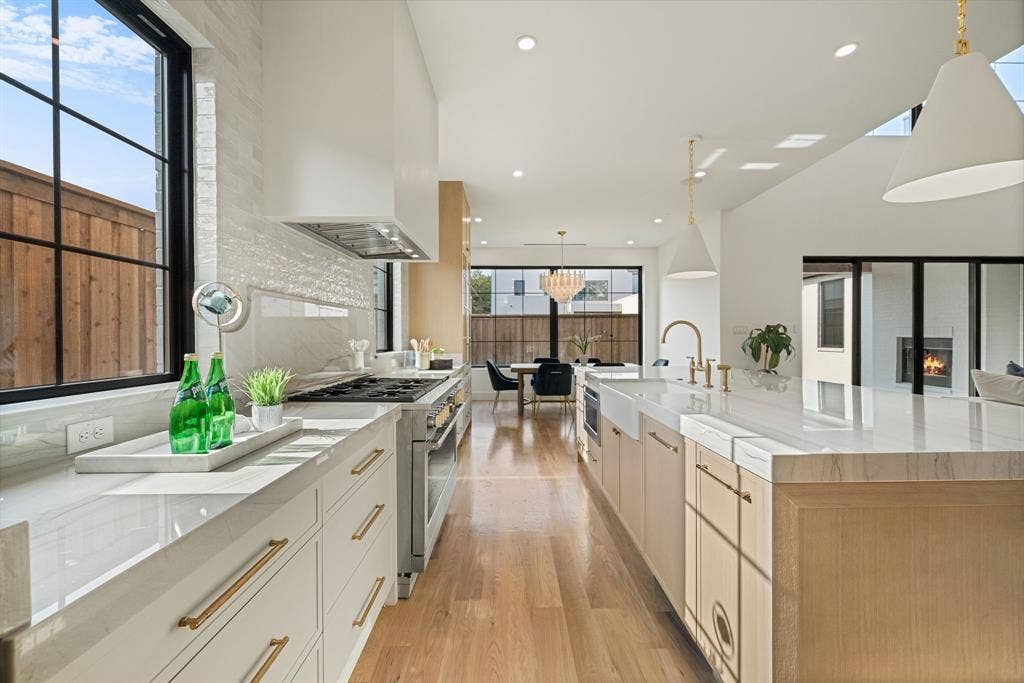 3723 Manana Drive, Dallas, TX 75220 Gourmet kitchen with extensive white countertops, a large center island with a farmhouse sink, stainless steel appliances, and wood-finish flooring