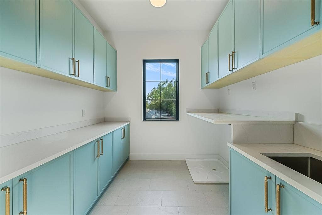 3723 Manana Drive, Dallas, TX 75220 Utility room featuring extensive light blue cabinetry with gold-toned hardware, light-toned countertops, a built-in sink, and a black-framed window