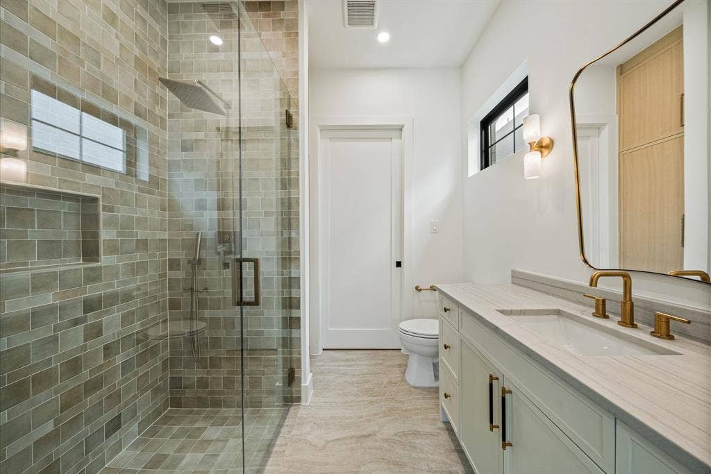 3723 Manana Drive, Dallas, TX 75220 Spa-inspired primary bathroom featuring a frameless glass-enclosed shower with subway tile surround, dual vanity with white quartz countertop, brass fixtures, and wood-finish flooring throughout
