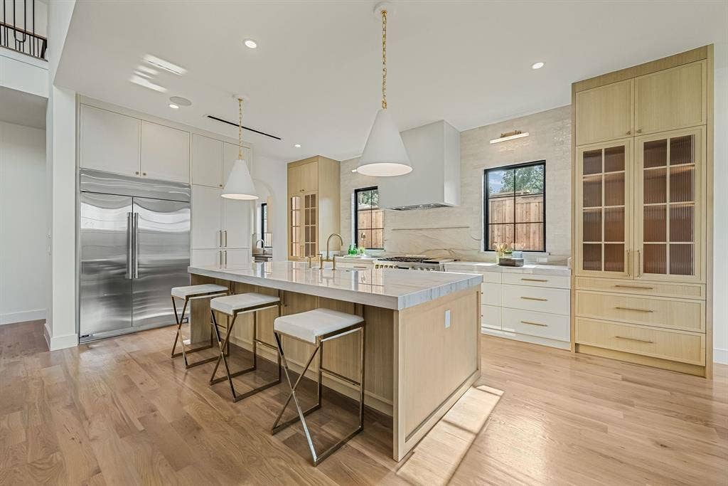 3723 Manana Drive, Dallas, TX 75220 Gourmet kitchen featuring a large central island with seating, stainless steel refrigerator, light wood-finish cabinetry, white countertop surfaces, and wood-finish flooring