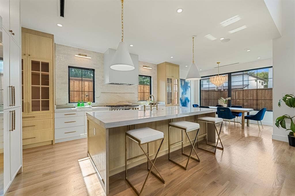 3723 Manana Drive, Dallas, TX 75220 Spacious open-concept kitchen featuring light wood-finish flooring, a large central island with seating, pendant lighting, built-in cabinetry with glass-front accents, and a dining area with a chandelier