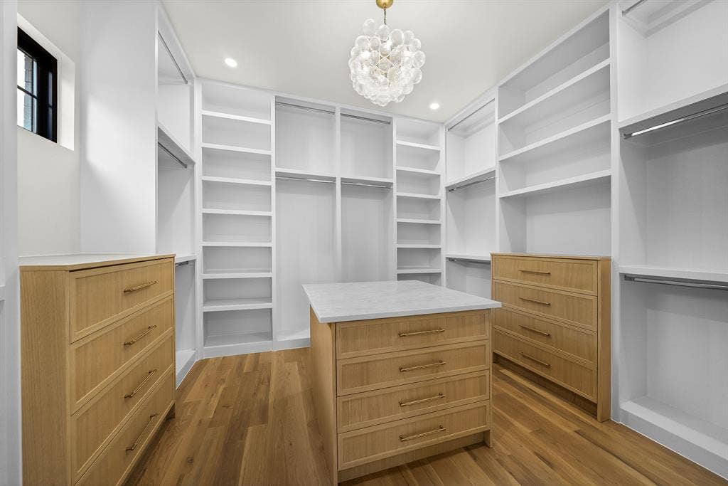 3723 Manana Drive, Dallas, TX 75220 Spacious custom closet featuring extensive built-in shelving, hanging rods, two integrated dressers, a central island with countertop, and wood-finish flooring