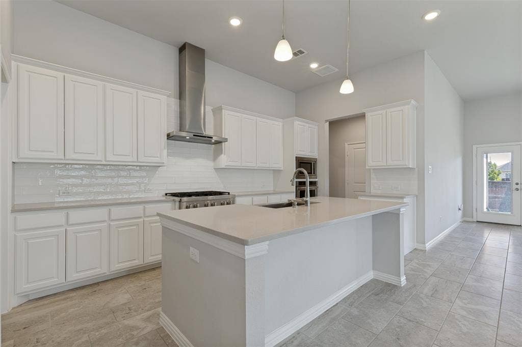 12464 Lost Valley Drive, Frisco, TX 75035 Bright kitchen featuring a central island with an undermount sink, white shaker cabinetry, a subway tile backsplash, a stainless steel range hood, and tile flooring