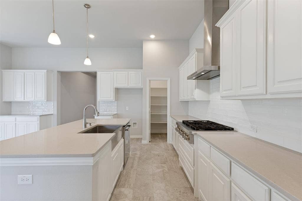 12464 Lost Valley Drive, Frisco, TX 75035 Spacious kitchen featuring white cabinetry, light-toned countertops, a professional-style 6-burner gas cooktop, a sleek modern vent hood, and a classic white subway tile backsplash