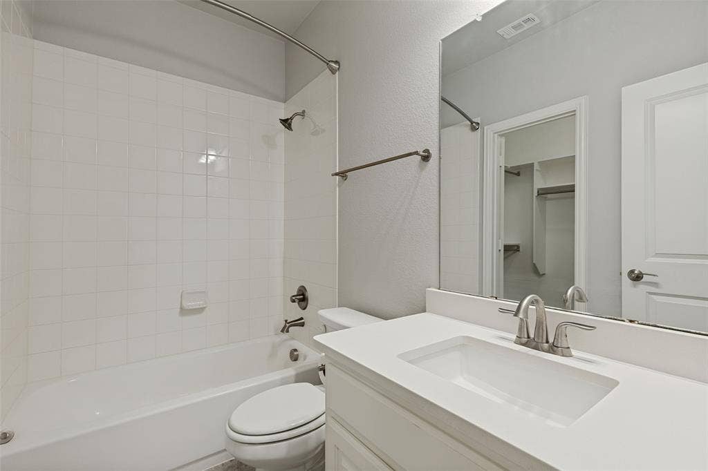 12464 Lost Valley Drive, Frisco, TX 75035 Full bathroom featuring a white tub with tile surround, a toilet, and a vanity with an integrated sink