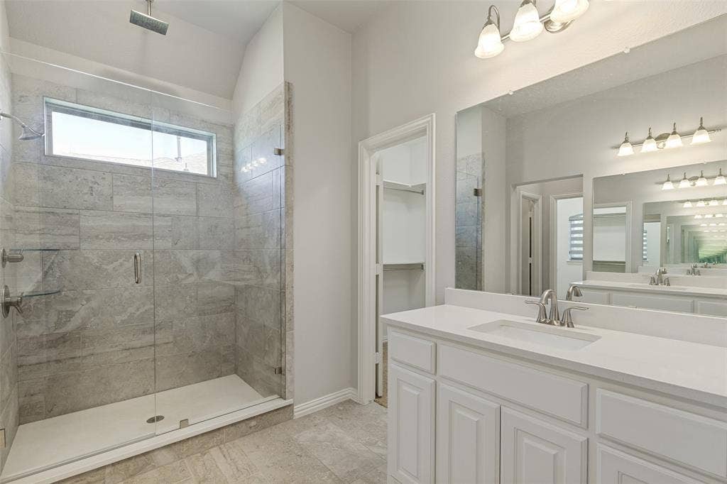 12464 Lost Valley Drive, Frisco, TX 75035 Spacious bathroom featuring a glass-enclosed shower with stone-look tile, transom window, dual vanity with white cabinetry, and a large wall-mounted mirror