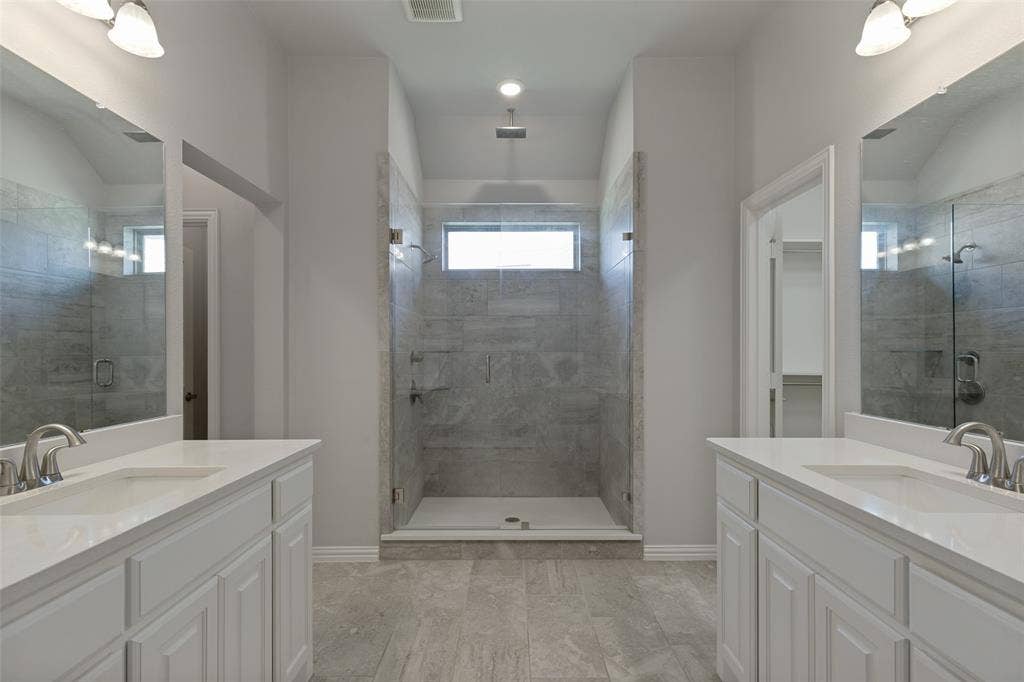 12464 Lost Valley Drive, Frisco, TX 75035 Spacious bathroom featuring a large walk-in shower with full-height tile surround, dual vanity sinks with white cabinetry, light-toned countertops, and brushed nickel fixtures