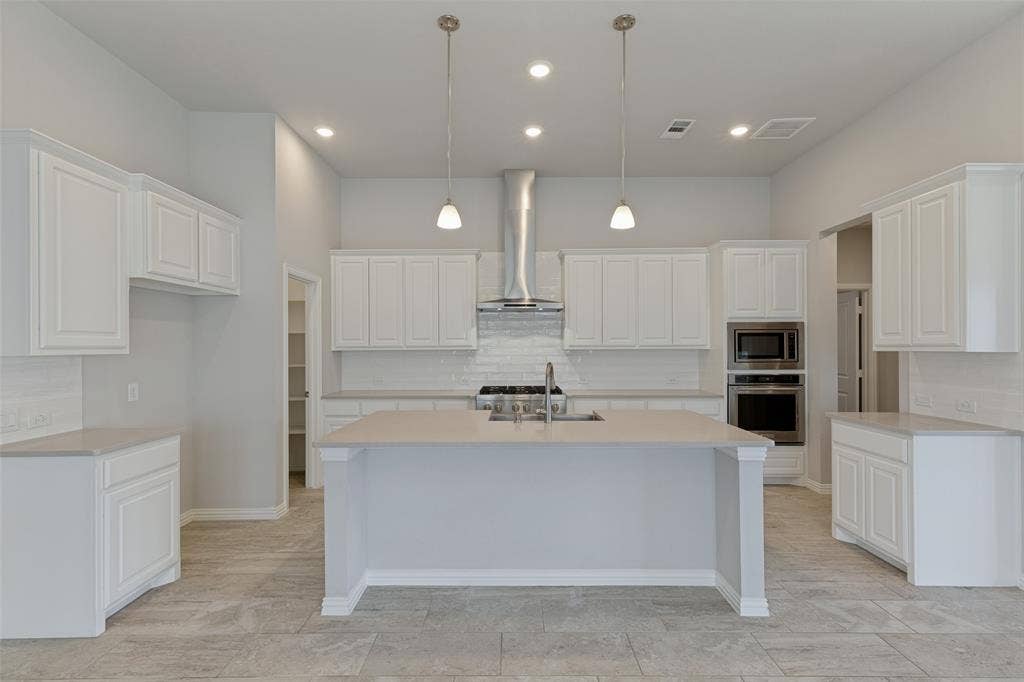 12464 Lost Valley Drive, Frisco, TX 75035 Modern kitchen featuring white shaker cabinetry, light-toned countertops, a central island with a sink, stainless steel appliances, and recessed lighting