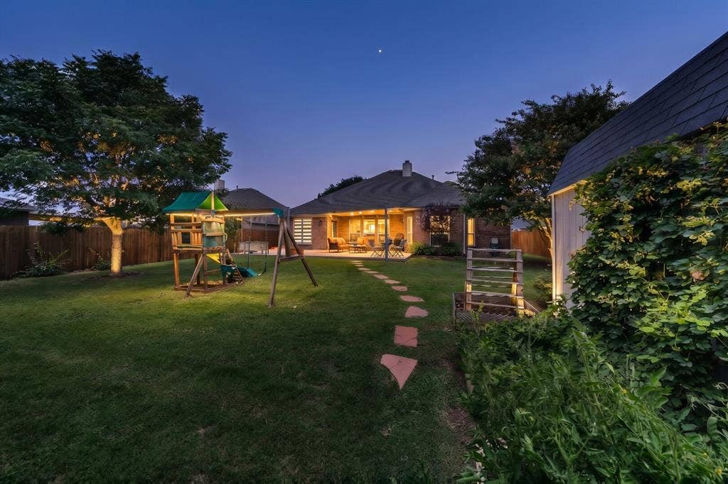 5304 Fox Run Drive, Watauga, TX 76137 As twilight settles in, this private backyard transforms into a peaceful retreat where soft landscape lighting (added as inspiration by photographer), a spacious covered patio, mature trees, and open green space create the perfect setting for entertaining, family gatherings, or quiet evenings under the stars.