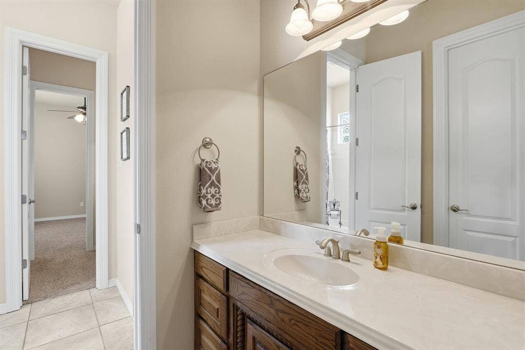 5030 Monroe Court, Midlothian, TX 76065 Bathroom vanity featuring a single-bowl sink, light-toned countertop, wood-finish cabinetry, and an expansive wall-mounted mirror