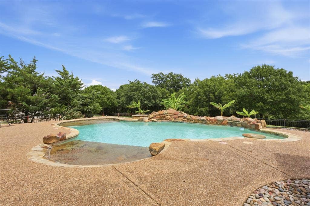 5030 Monroe Court, Midlothian, TX 76065 Freeform swimming pool featuring a rock waterfall, integrated spa, and an expansive exposed aggregate patio