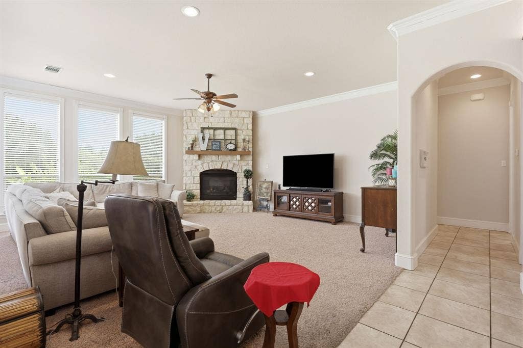 5030 Monroe Court, Midlothian, TX 76065 Spacious living area featuring a stone fireplace, crown molding, abundant natural light from multiple windows, recessed lighting, and an arched entryway