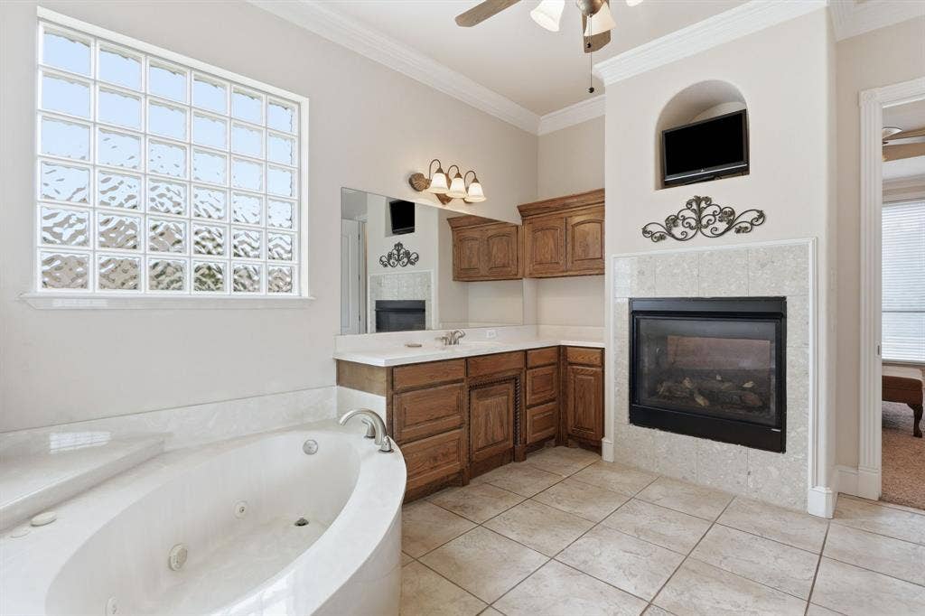 5030 Monroe Court, Midlothian, TX 76065 Soaking tub with integrated jets, glass block window, double vanity with wood cabinetry, tiled flooring, and a fireplace with a tiled surround