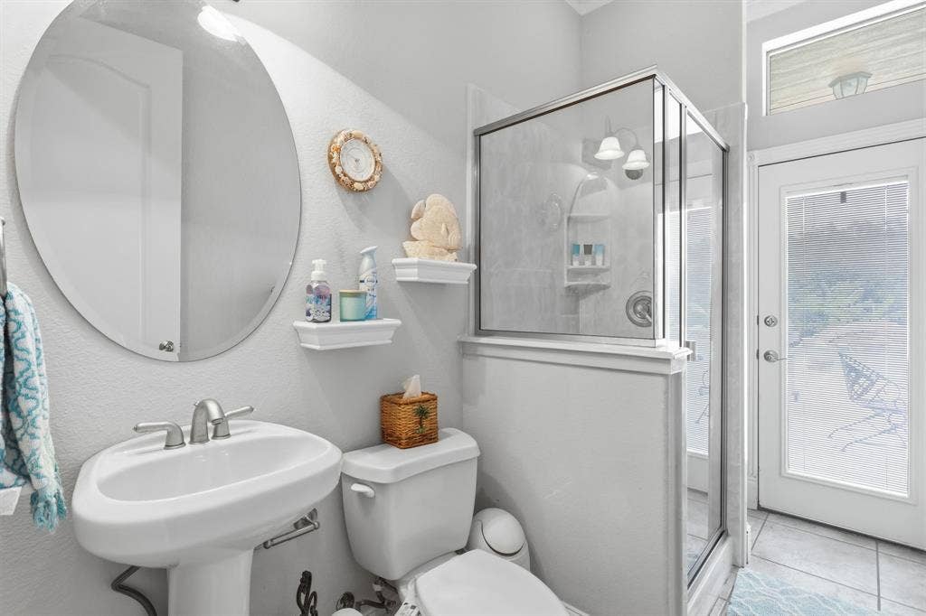5030 Monroe Court, Midlothian, TX 76065 Pedestal sink with a brushed nickel faucet, large oval mirror, glass-enclosed shower with tiled walls, and a full-light exterior door