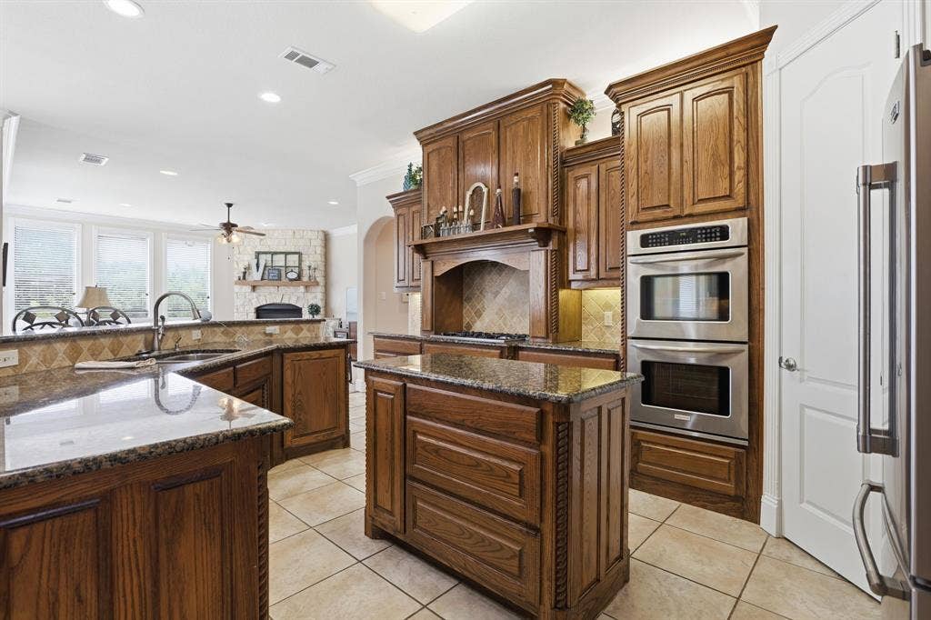 5030 Monroe Court, Midlothian, TX 76065 Kitchen featuring rich wood cabinetry, granite countertops, a central island, stainless steel double ovens, and tile flooring