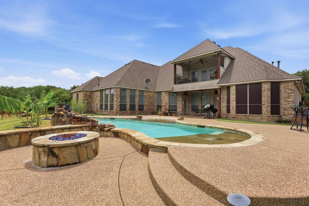5030 Monroe Court, Midlothian, TX 76065 Expansive exposed aggregate patio surrounding a freeform swimming pool with integrated rock waterfall feature