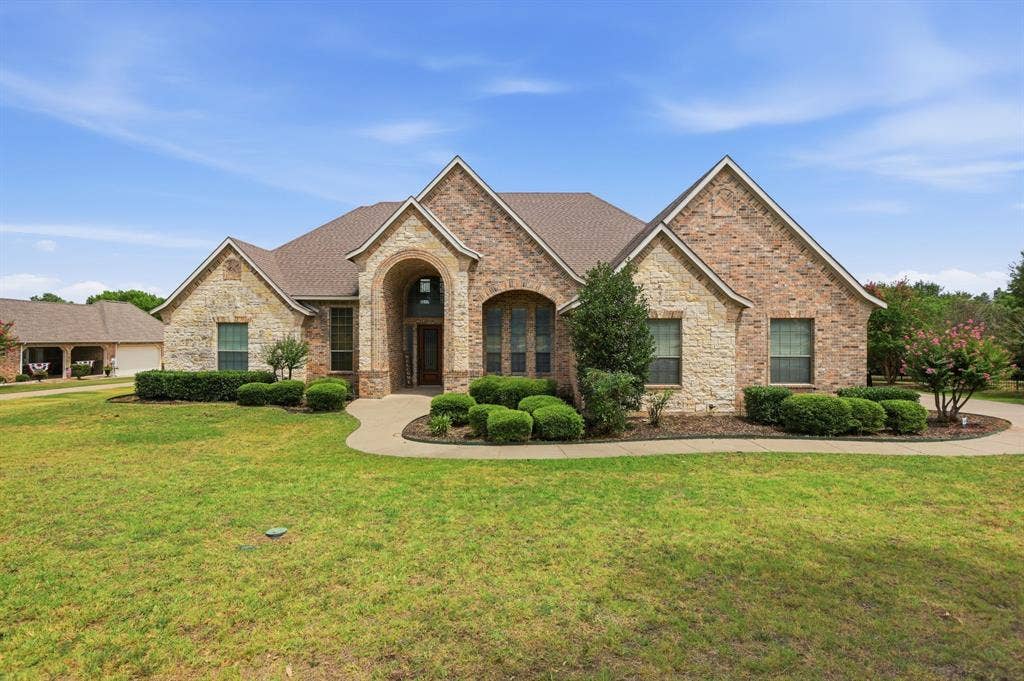 5030 Monroe Court, Midlothian, TX 76065 Brick and stone facade residence featuring a covered entry, arched windows, and a concrete pathway leading to the front door