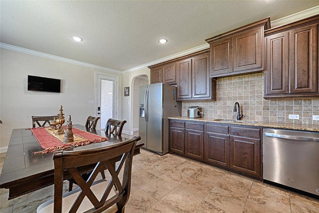 2nd Kitchen and dining area featuring dark wood-finish cabinetry, stainless steel appliances, a mosaic tile backsplash, and light-toned tile flooring