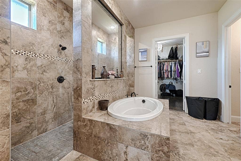 Spacious bathroom featuring an oval built-in soaking tub, a walk-in shower with tiled walls and a mosaic accent, and a separate walk-in closet with built-in shelving