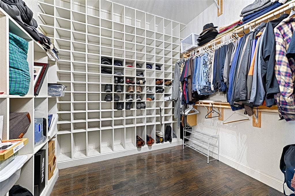 Custom closet featuring extensive cubby shelving, hardwood-finish flooring, white walls, built-in clothing rods, and baseboard trim