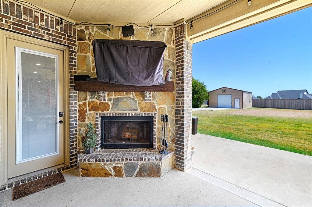 Covered outdoor patio featuring a stone fireplace with a wood mantel