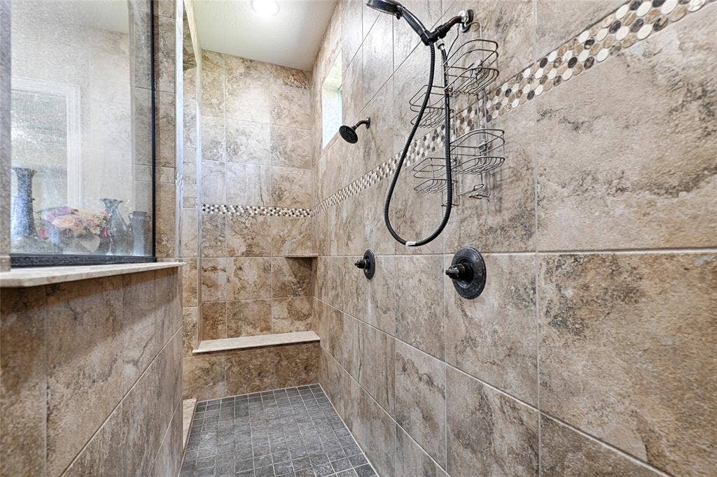 Tiled shower with a built-in bench, recessed shelf, mosaic accent banding, and a handheld shower fixture