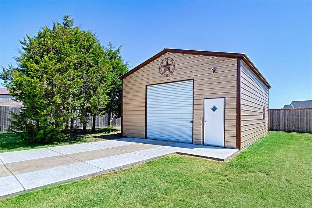 Metal utility building featuring a corrugated roll-up door, an access door with a diamond-shaped window, and a concrete driveway