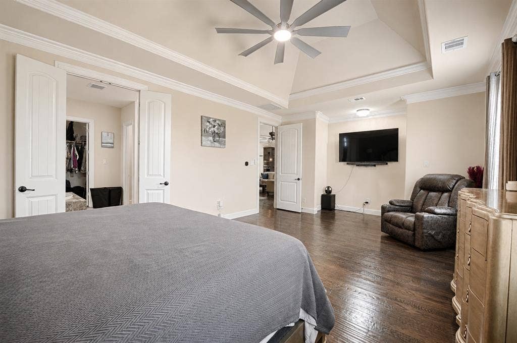Spacious room featuring dark wood-finish flooring, a tray ceiling with crown molding, and a ceiling fan