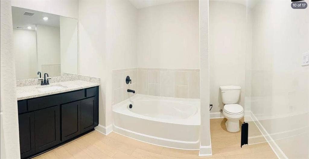 1323 windermere Way, Princeton, TX 75407 Bathroom featuring a dark wood-finish vanity with a light speckled countertop, a white soaking tub with black fixtures, and light wood-finish flooring