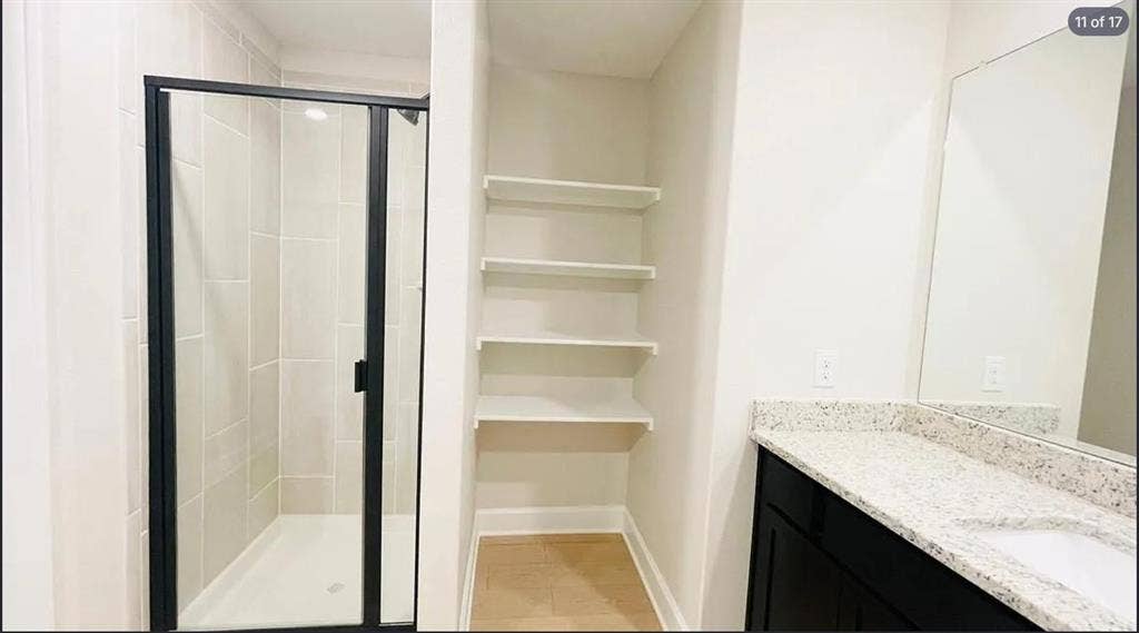 1323 windermere Way, Princeton, TX 75407 Bathroom featuring a glass-enclosed shower with tiled walls, built-in shelving, and a vanity with a light-toned countertop and dark cabinetry