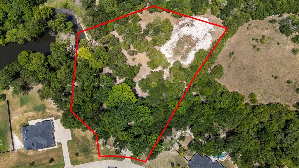 Expansive undeveloped land parcel outlined in red, featuring mature tree coverage, a clearings, and a natural water body along one boundary