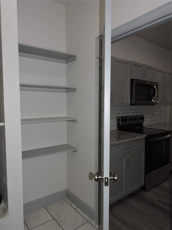 6110 Tejas Drive, Mabank, TX 75156 Pantry with built-in shelving and tile flooring, opening to a kitchen featuring grey cabinetry, stainless steel appliances, and granite countertops