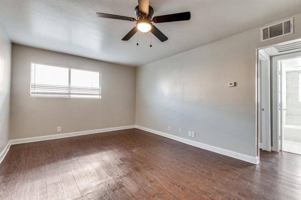 4915 Reiger Avenue, #D, Dallas, TX 75214 Spacious room with wood-finish flooring, a ceiling fan with integrated lighting, and a large window featuring horizontal blinds