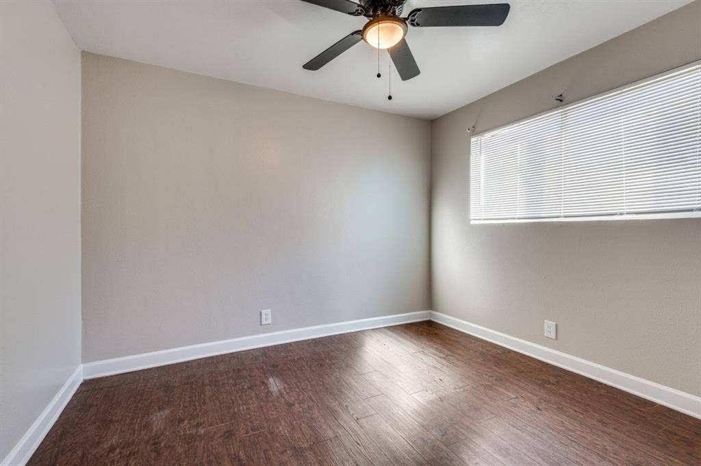4915 Reiger Avenue, #D, Dallas, TX 75214 Spacious room featuring wood-finish flooring, light grey painted walls, white baseboards, and a ceiling fan with integrated lighting