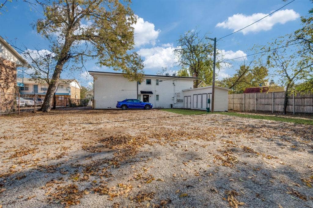 4915 Reiger Avenue, #D, Dallas, TX 75214 Gravel parking area featuring mature trees and a privacy fence bordering the property