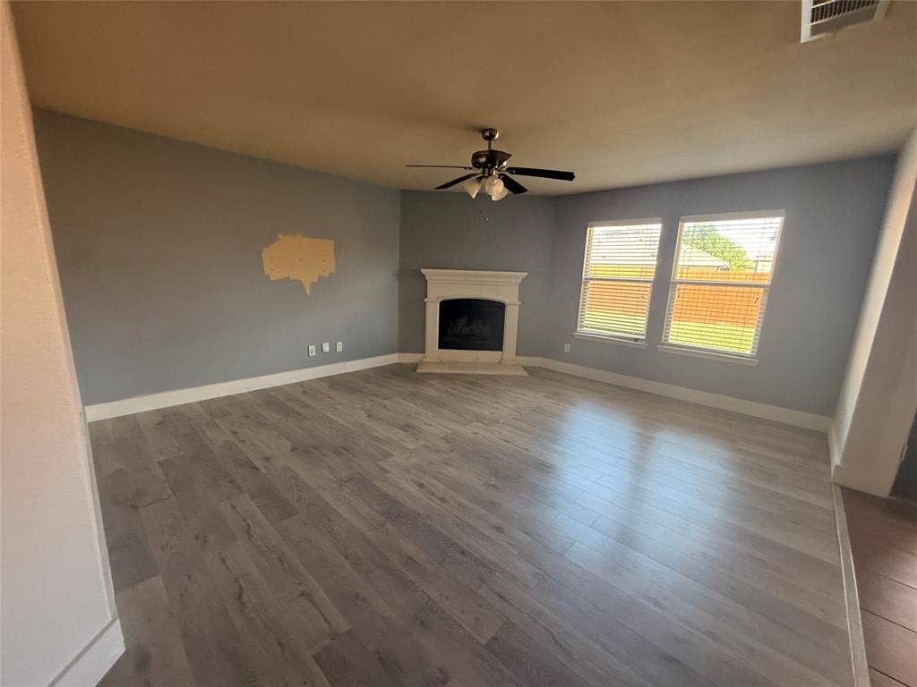2004 Samantha Lane, Heartland, TX 75126 Living area featuring wood-finish flooring, a fireplace with a decorative mantel, multiple windows with blinds, a ceiling fan with integrated lighting, and painted walls
