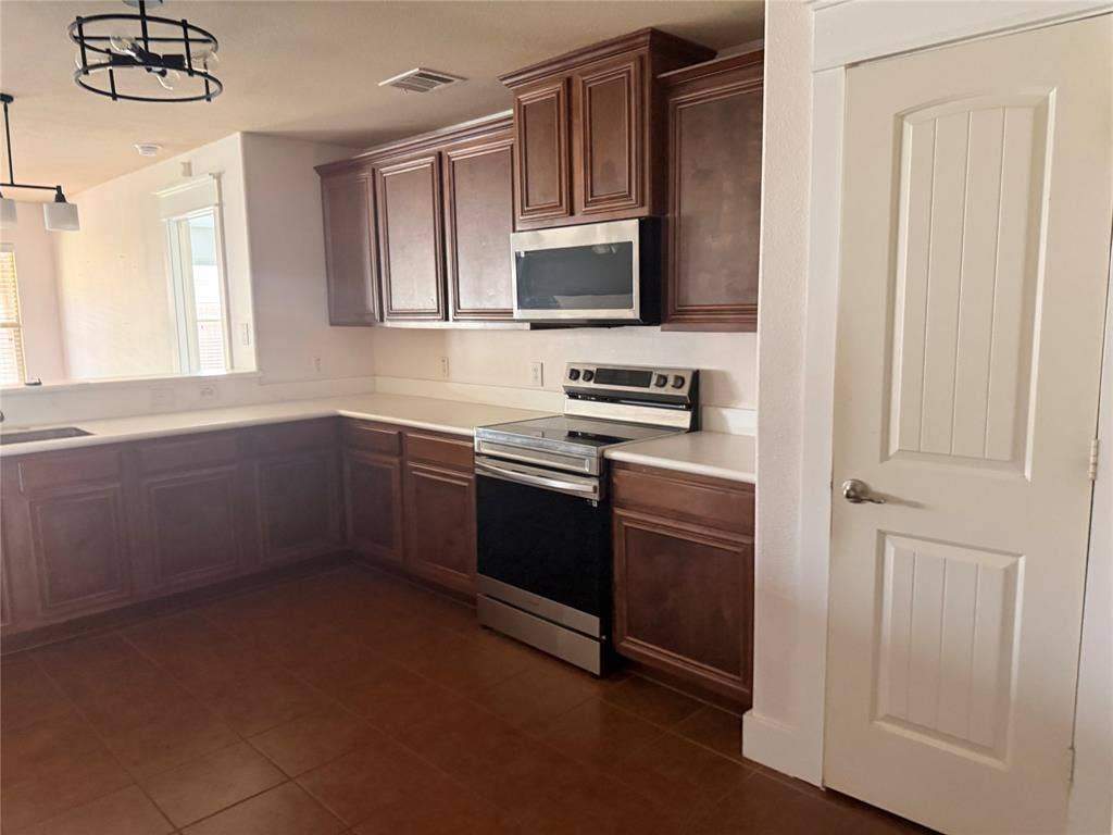 2004 Samantha Lane, Heartland, TX 75126 Kitchen featuring wood-finish cabinetry, light-toned countertops, and stainless steel appliances including a range and built-in microwave