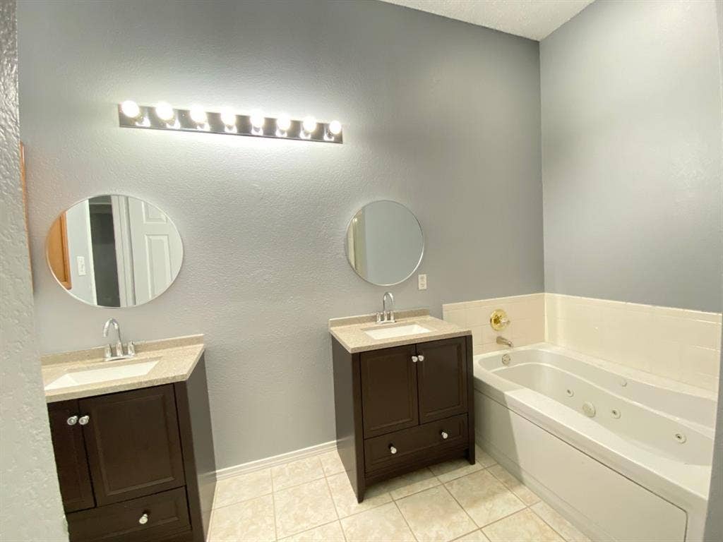1328 Falcon Hollow, Cedar Hill, TX 75104 Bathroom featuring dual dark wood vanities with light-toned countertops, two circular mirrors, and a built-in jetted tub