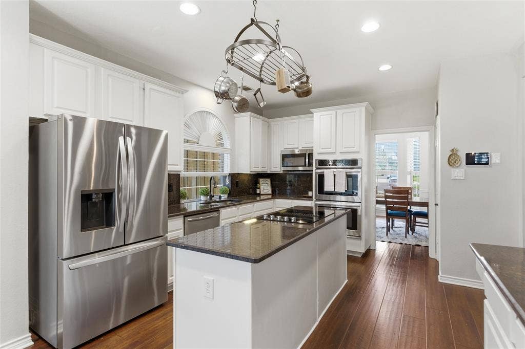 4112 Blackpool Drive, Plano, TX 75093 Gourmet kitchen featuring white cabinetry, stainless steel appliances, dark stone countertops, wood-finish flooring, and a central island with a cooktop