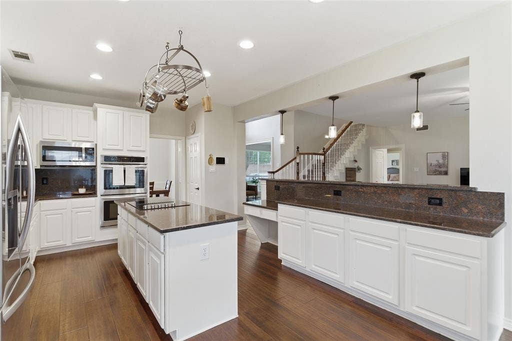 4112 Blackpool Drive, Plano, TX 75093 Kitchen featuring white cabinetry, dark stone countertops, stainless steel appliances, wood-finish flooring, and a central island with cooktop