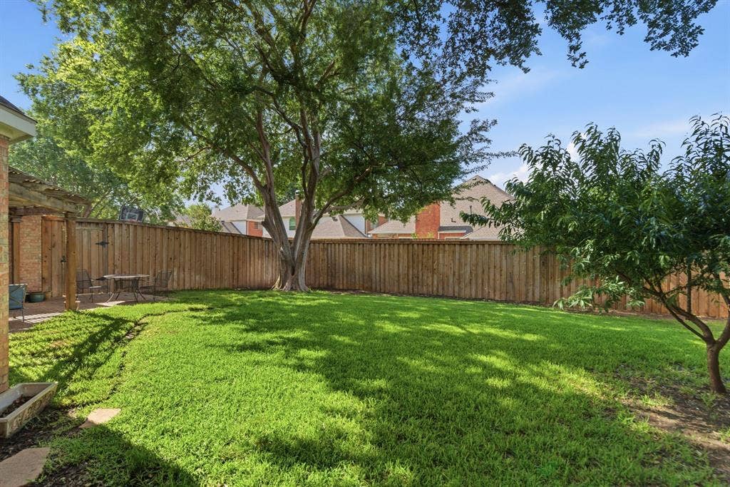 4112 Blackpool Drive, Plano, TX 75093 Expansive backyard featuring a large tree, lush green lawn, private wood fencing, and a brick patio with a pergola structure