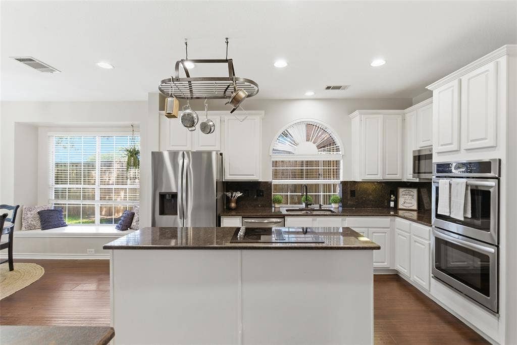 4112 Blackpool Drive, Plano, TX 75093 White cabinetry kitchen featuring a central island, stainless steel appliances, dark countertops, and wood-finish flooring
