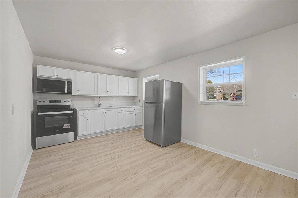 9021 White Settlement Road, #D, White Settlement, TX 76108 Kitchen featuring white cabinetry, light countertops, wood-finish flooring, a stainless steel refrigerator, and a stainless steel oven with an overhead microwave
