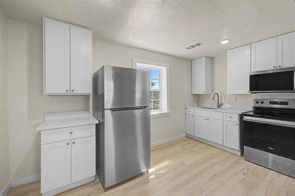 9021 White Settlement Road, #D, White Settlement, TX 76108 Kitchen featuring light wood-finish flooring, white cabinetry, light-toned countertops, a stainless steel refrigerator, and a stainless steel range with an overhead microwave
