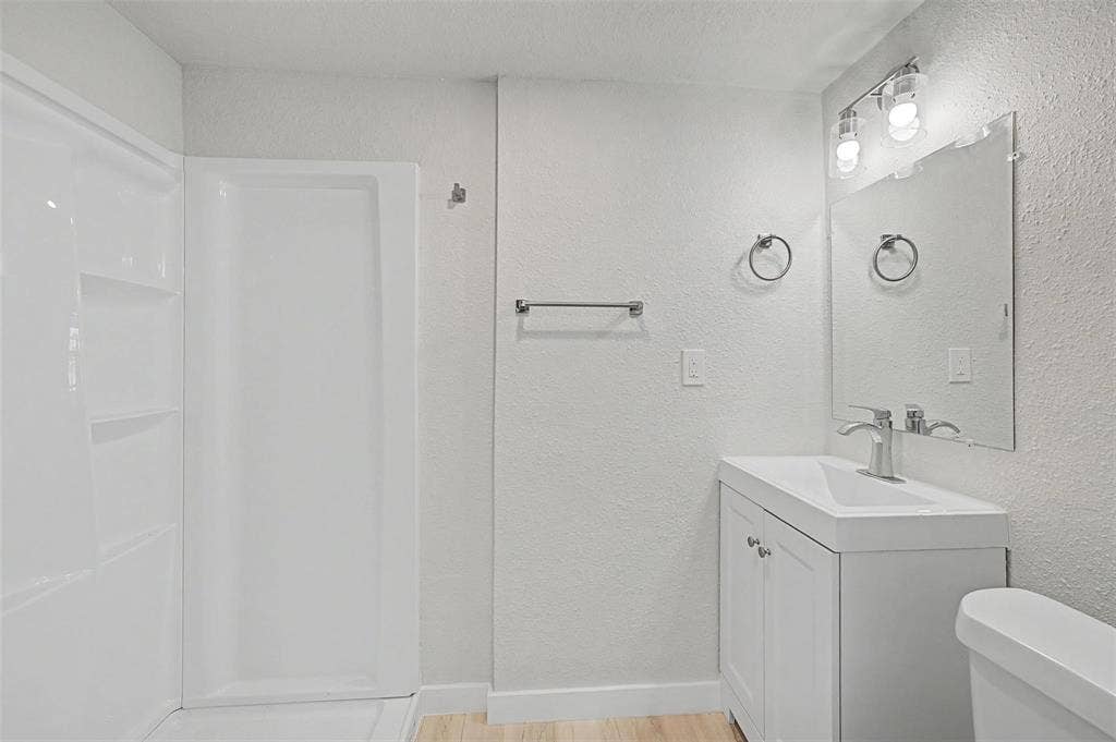 9021 White Settlement Road, #D, White Settlement, TX 76108 Full bathroom featuring a walk-in shower with built-in shelving, a single vanity with a white basin sink and chrome faucet, and wood-finish flooring