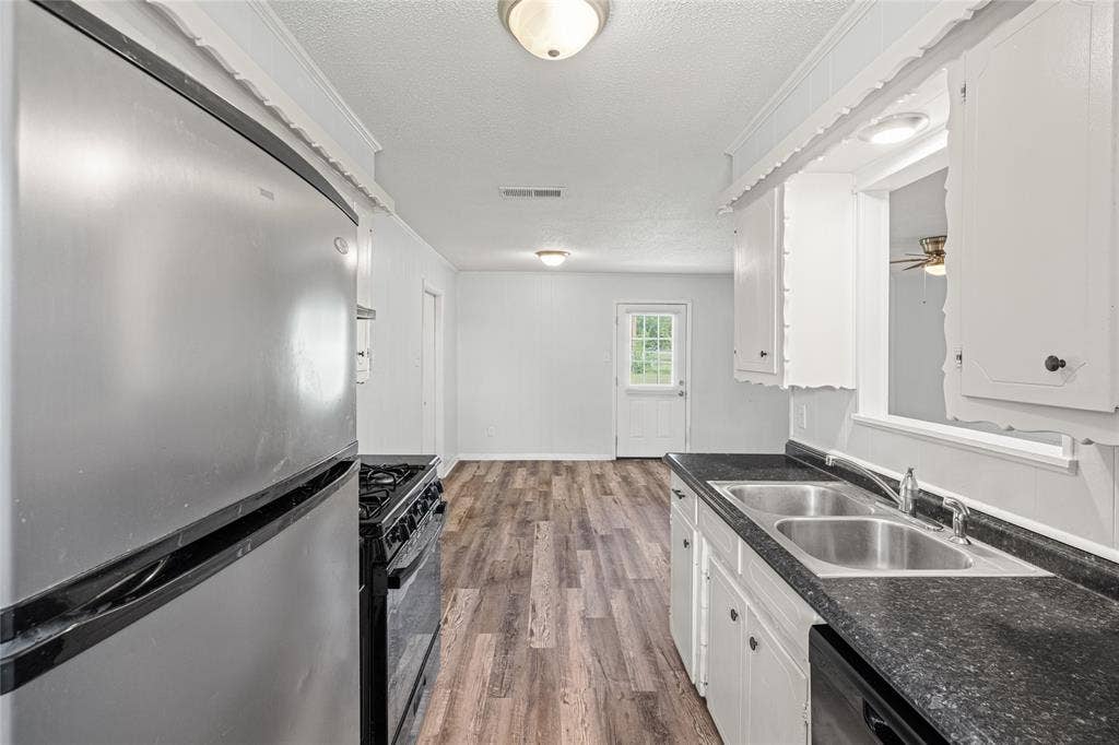 3407 Highmeadow Lane, Greenville, TX 75402 Kitchen featuring a stainless steel refrigerator, black gas range, dual basin stainless steel sink, black countertops, and white cabinetry