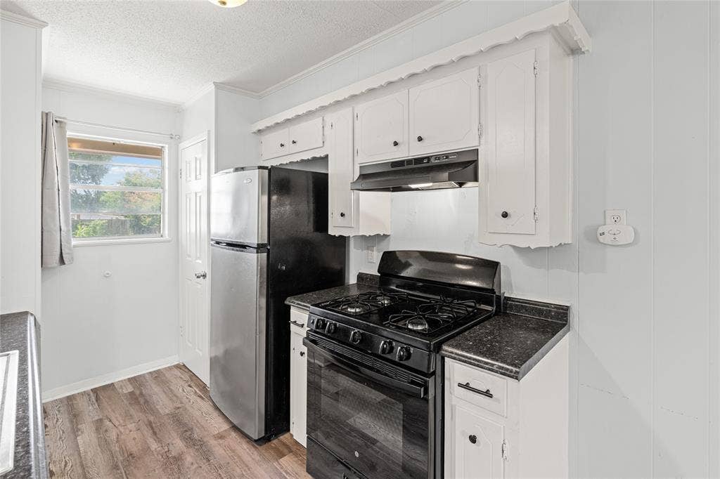3407 Highmeadow Lane, Greenville, TX 75402 Kitchen featuring white cabinetry, black countertops, a stainless steel refrigerator, a black gas range, and wood-finish flooring