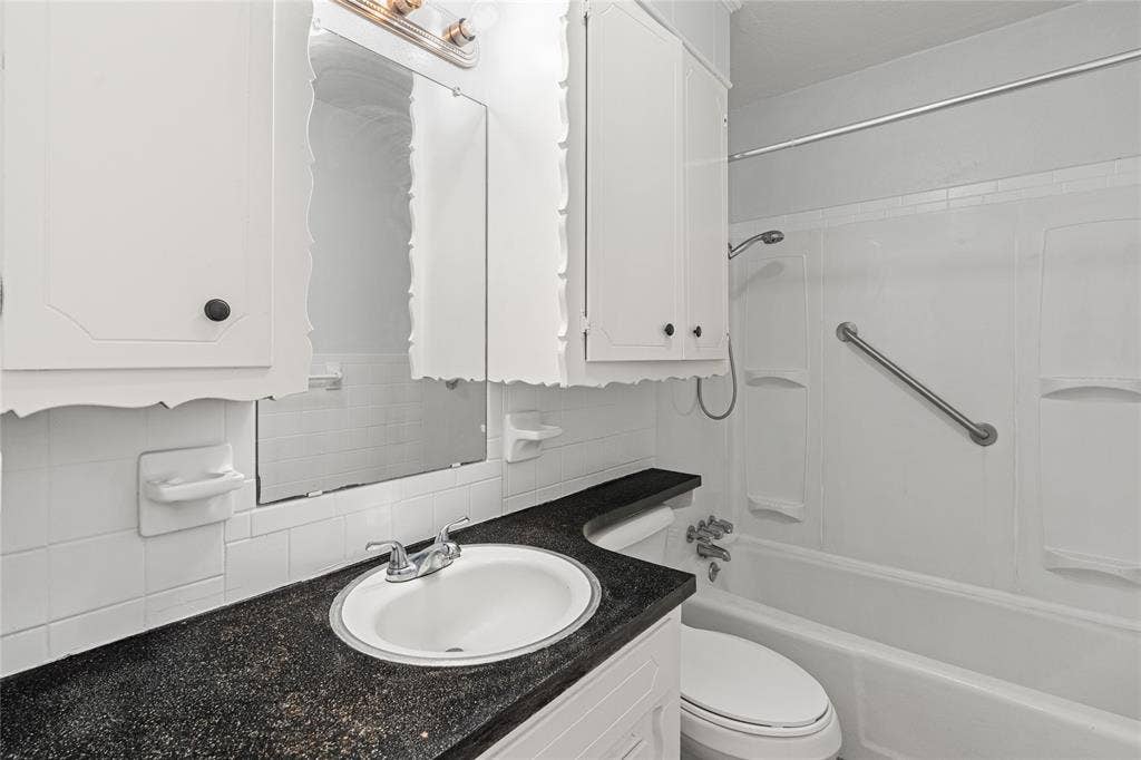 3407 Highmeadow Lane, Greenville, TX 75402 White bathroom featuring a built-in tub with a shower head, grab bar, and wall-mounted shower caddy