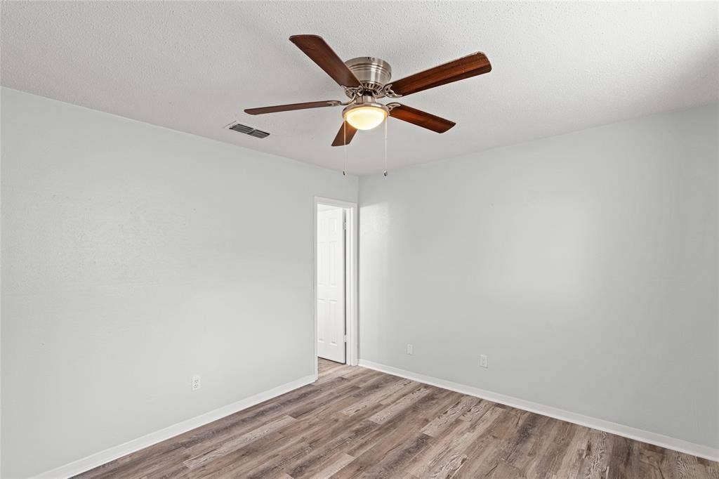 3407 Highmeadow Lane, Greenville, TX 75402 Room featuring wood-finish flooring, light grey walls, white baseboards, and a ceiling fan with integrated lighting
